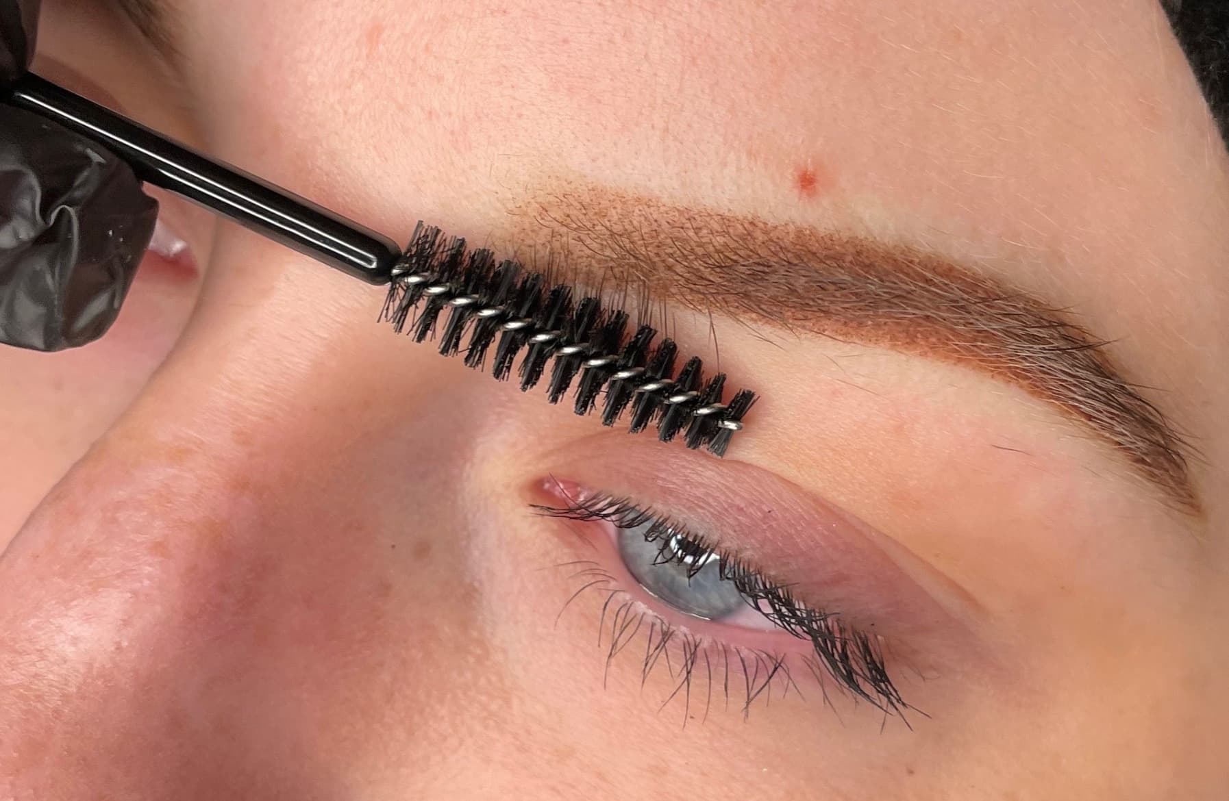 Macro of a healed ombré powder brow with a spoolie brush mid-grooming — soft powder gradient, light skin, real client